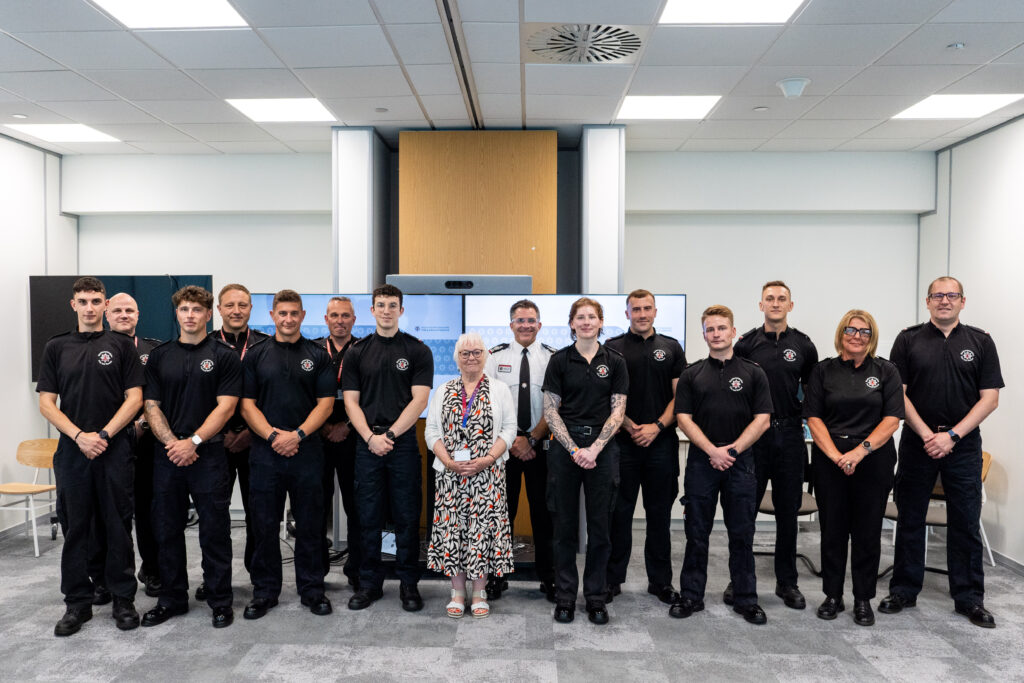 A number of apprentices and firefighter staff are shown pictured in a group wearing black uniform an office setting. In the middle of the group, wearing non-uniform, is Police, Fire and Crime Commissioner Danielle Stone, while pictured immediately to her right, in a white shirt uniform, is Deputy Chief Fire Officer Simon Tuhill.