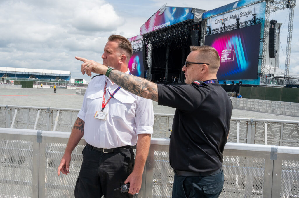 Neil King, of the Joint Operations Team, is shown wearing a black tee shirt and pointing in the direction of something he is making his colleague. Group Commander Matt Butler - who is wearing white - aware of.