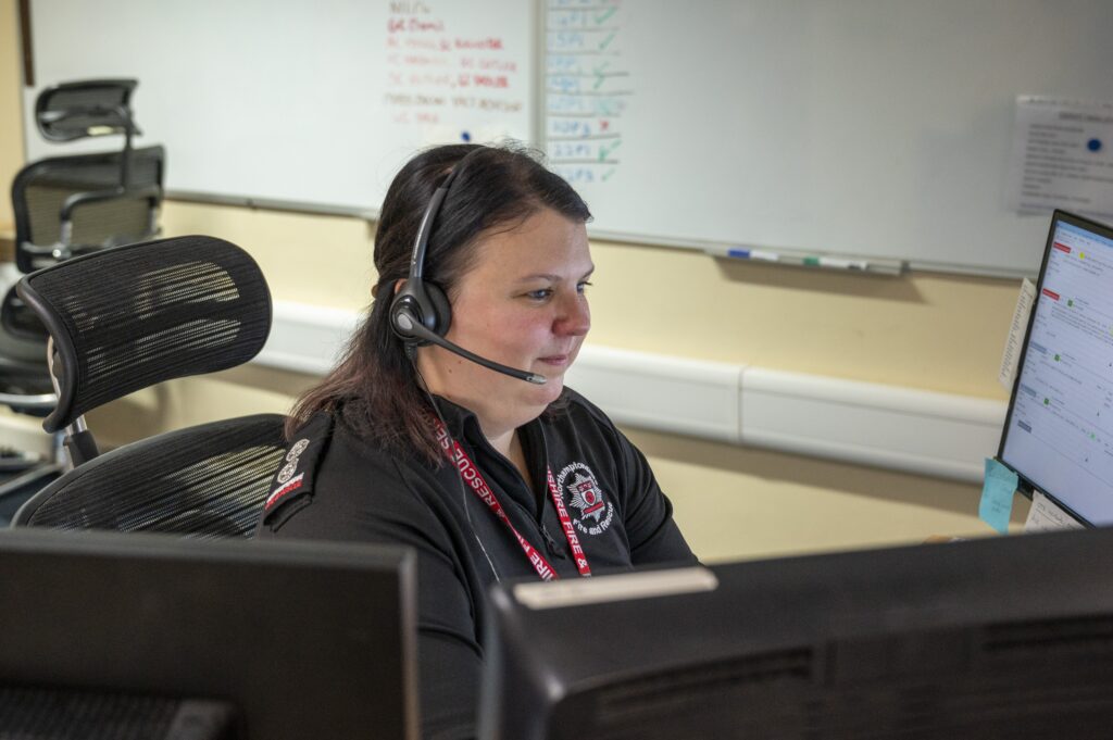 Hayleigh Marks Tabalis sitting at computer desk, wearing a black top with NFRS logo on it and a headset