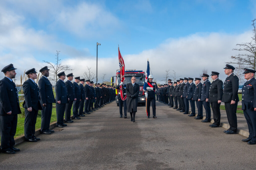 Two flag bearers in front of a fire engine going through a guard of honour