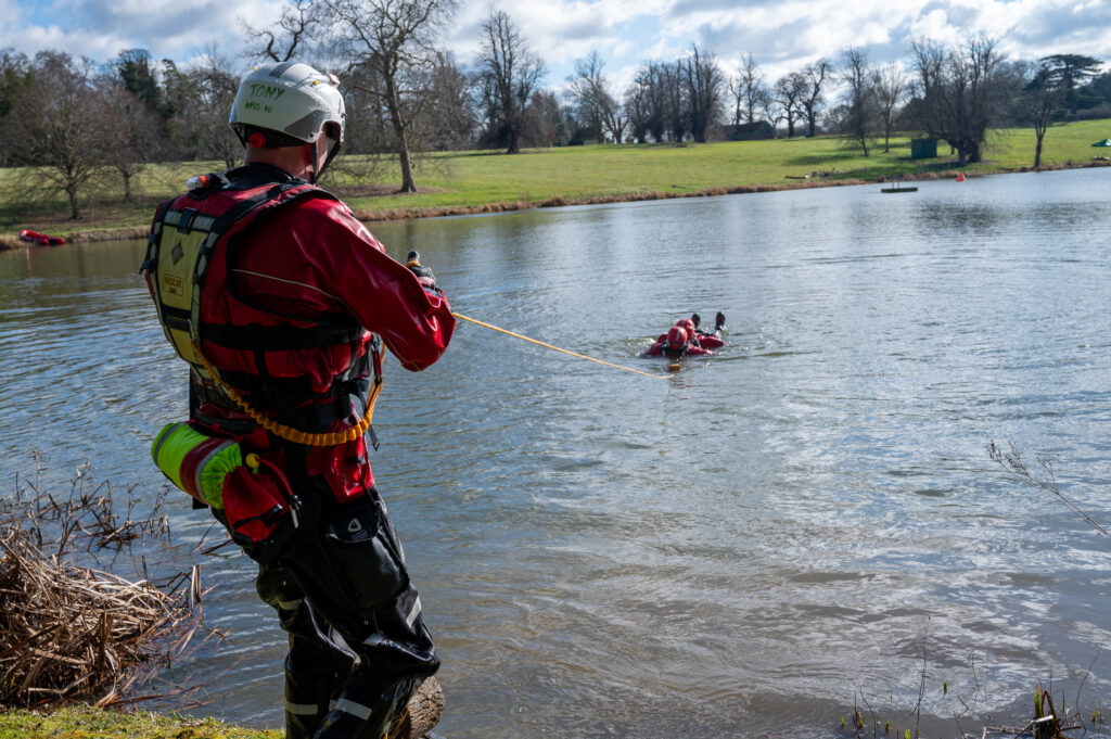 A firefighter in full water safety kit, using a throwline to pull two other firefighters out of the water during a drill